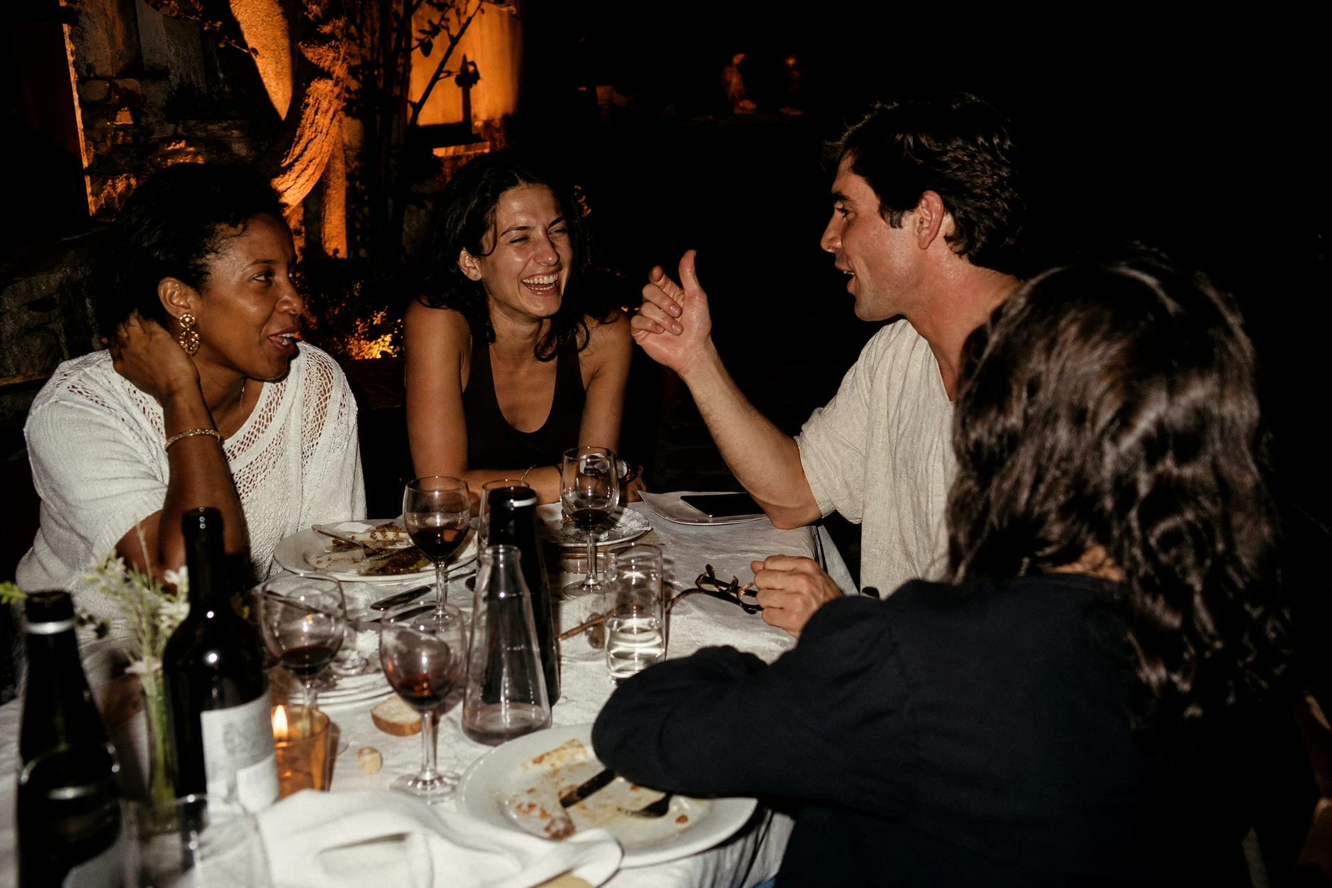 Candid direct-flash photograph of people talking animatedly around a table at an evening gathering